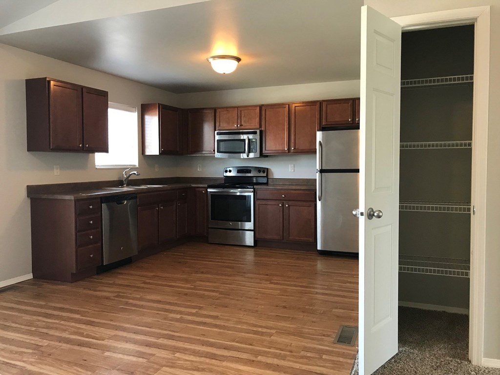 an empty kitchen with wooden floors and stainless steel appliances